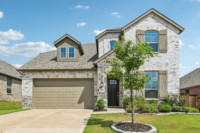 french country inspired facade featuring stone siding, a front lawn, an attached garage, and driveway