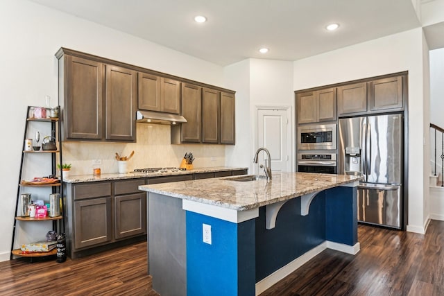 kitchen featuring light stone countertops, appliances with stainless steel finishes, dark wood-type flooring, sink, and a kitchen island with sink