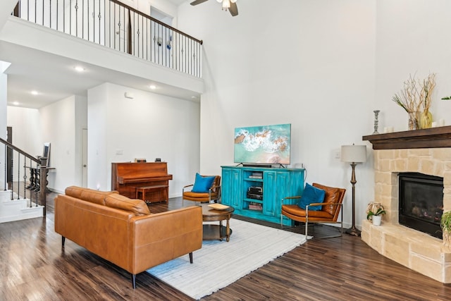 living room featuring ceiling fan, hardwood / wood-style flooring, a towering ceiling, and a stone fireplace