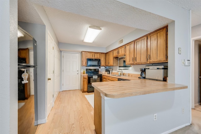 kitchen featuring kitchen peninsula, sink, light hardwood / wood-style floors, a textured ceiling, and black appliances