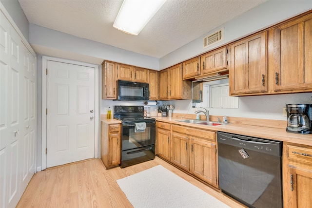 kitchen with sink, black appliances, a textured ceiling, and light wood-type flooring