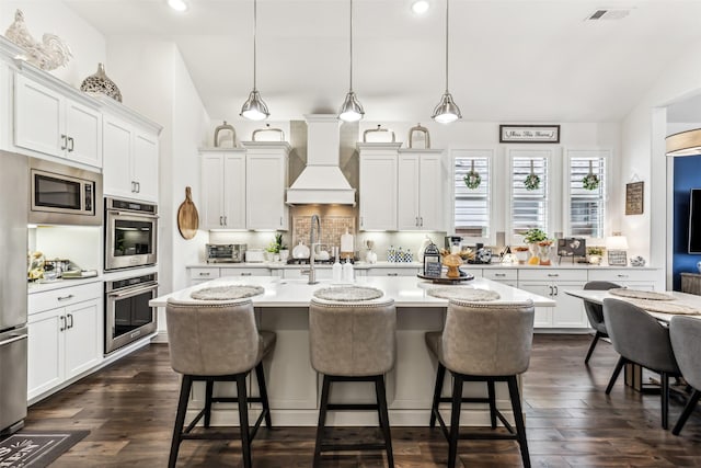 kitchen with decorative light fixtures, an island with sink, white cabinets, and custom exhaust hood