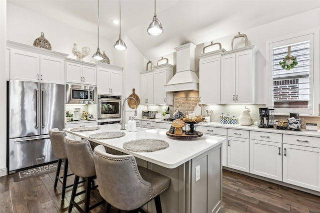 kitchen featuring appliances with stainless steel finishes, decorative light fixtures, custom exhaust hood, backsplash, and a center island with sink