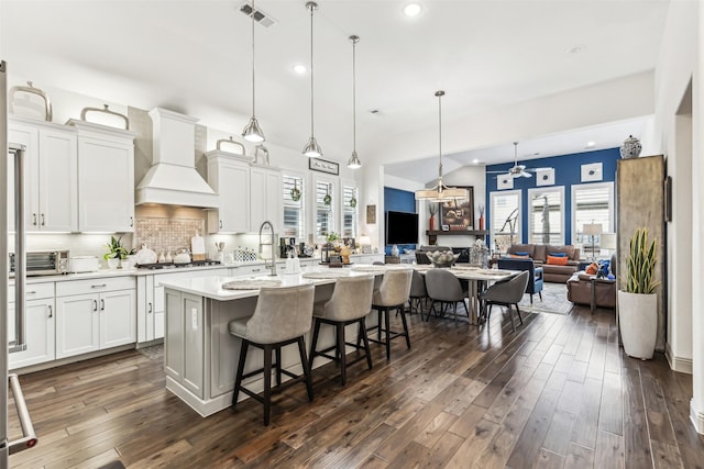 kitchen with a kitchen breakfast bar, pendant lighting, custom range hood, white cabinets, and a kitchen island with sink