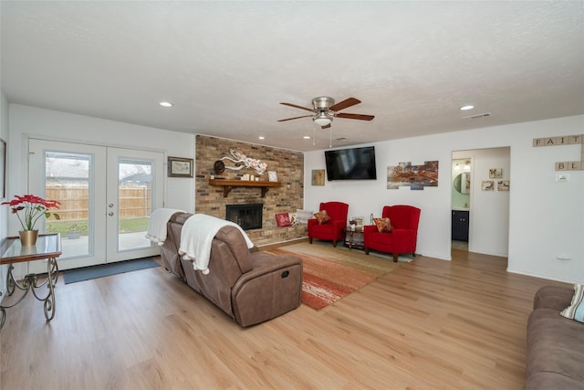 living room featuring french doors, light hardwood / wood-style flooring, a fireplace, and a textured ceiling