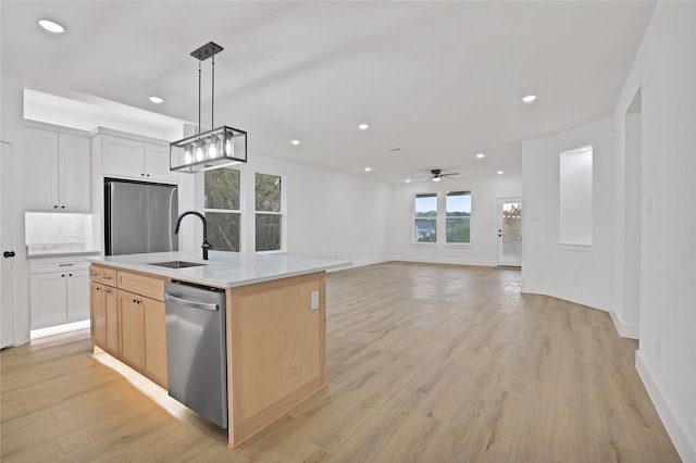 kitchen featuring appliances with stainless steel finishes, decorative light fixtures, white cabinetry, sink, and a center island with sink