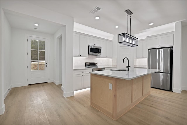 kitchen with appliances with stainless steel finishes, white cabinetry, hanging light fixtures, sink, and an island with sink