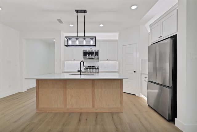 kitchen with stainless steel appliances, white cabinetry, a kitchen island with sink, and pendant lighting