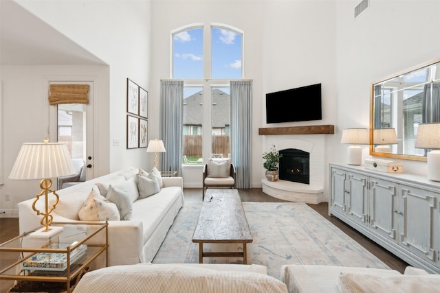 living area with baseboards, visible vents, dark wood finished floors, a towering ceiling, and a fireplace