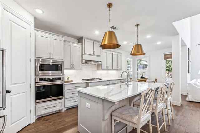 kitchen with appliances with stainless steel finishes, decorative light fixtures, a kitchen bar, dark hardwood / wood-style flooring, and an island with sink