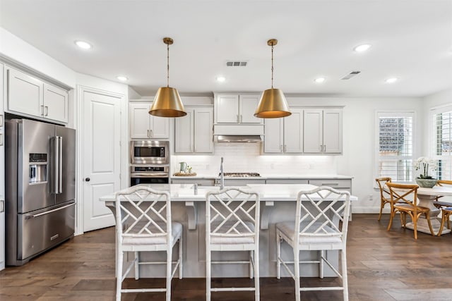 kitchen featuring dark wood finished floors, stainless steel appliances, light countertops, visible vents, and decorative backsplash