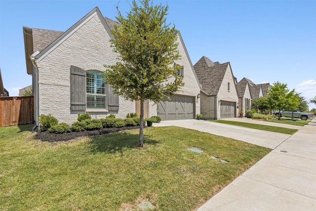 french country home featuring stone siding, a front yard, concrete driveway, and fence