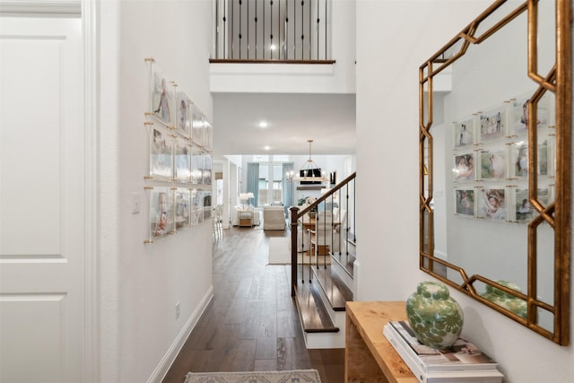 hall featuring a towering ceiling, stairway, baseboards, and wood finished floors