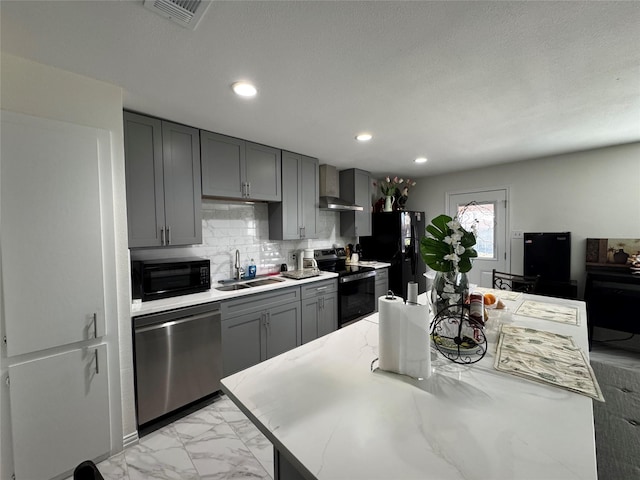 kitchen featuring sink, backsplash, gray cabinetry, wall chimney range hood, and black appliances