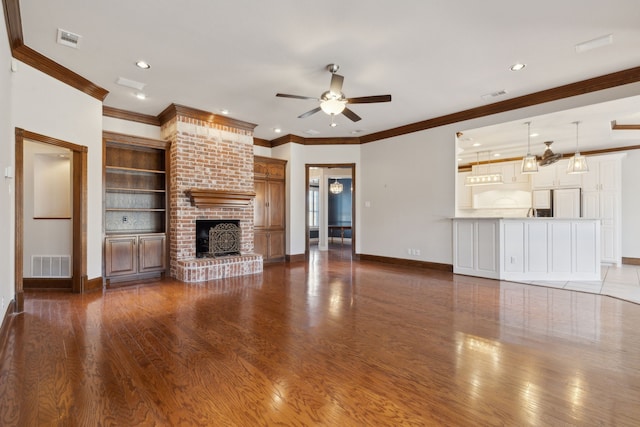 unfurnished living room with crown molding, a fireplace, built in shelves, dark hardwood / wood-style flooring, and ceiling fan