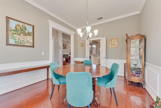 dining room with a fireplace, hardwood / wood-style floors, a notable chandelier, and ornamental molding