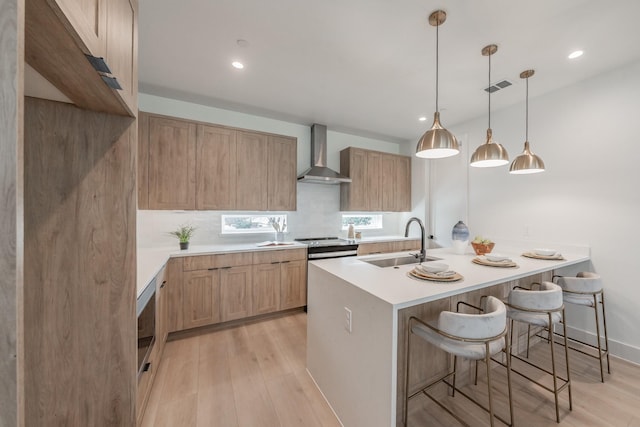 kitchen featuring light hardwood / wood-style flooring, sink, decorative light fixtures, a kitchen bar, and wall chimney range hood