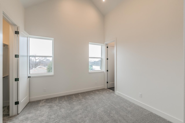 carpeted spare room with high vaulted ceiling