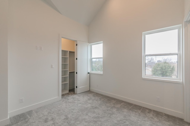 unfurnished bedroom with light colored carpet, a walk in closet, and vaulted ceiling