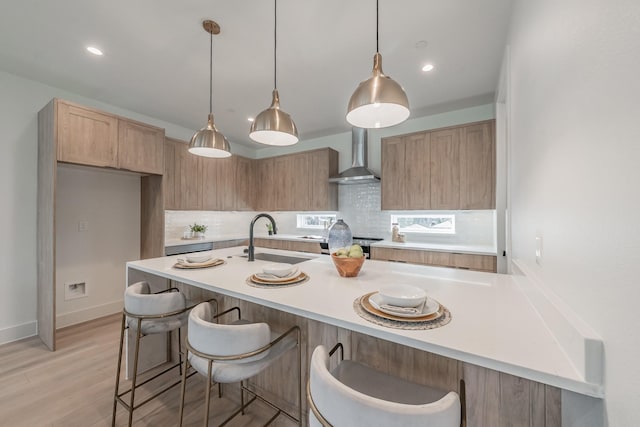 kitchen with light brown cabinetry, hanging light fixtures, decorative backsplash, wall chimney range hood, and sink