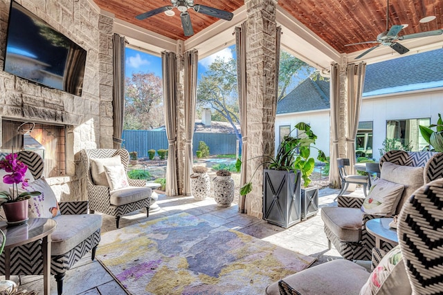 sunroom / solarium featuring ceiling fan, a stone fireplace, and wood ceiling