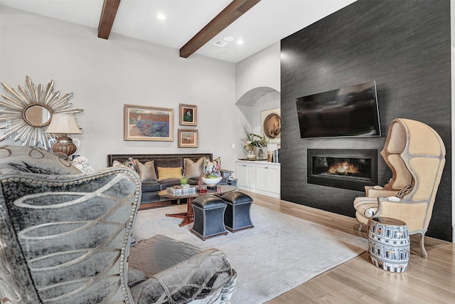 living room with light hardwood / wood-style floors, beamed ceiling, and a fireplace