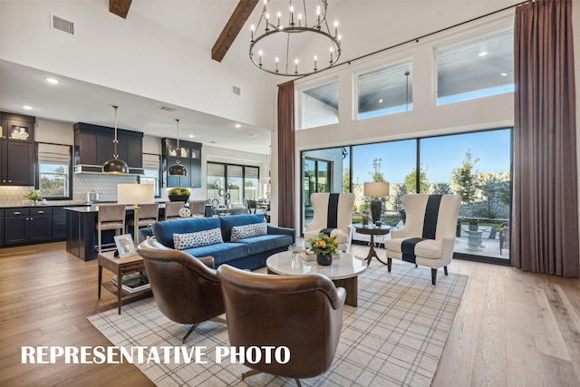 living room with a towering ceiling, beamed ceiling, light wood-type flooring, sink, and an inviting chandelier