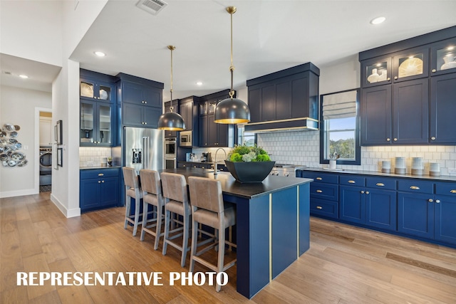 kitchen with light hardwood / wood-style flooring, decorative light fixtures, blue cabinets, a center island with sink, and a breakfast bar area