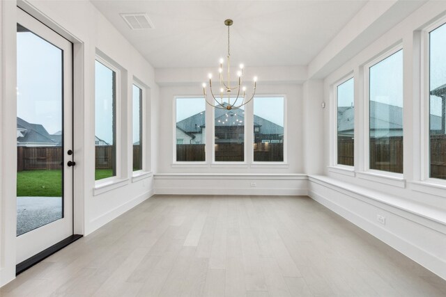 unfurnished sunroom with baseboards, a notable chandelier, wood finished floors, and visible vents