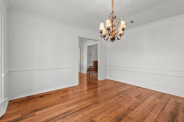 empty room featuring hardwood / wood-style floors, an inviting chandelier, and crown molding