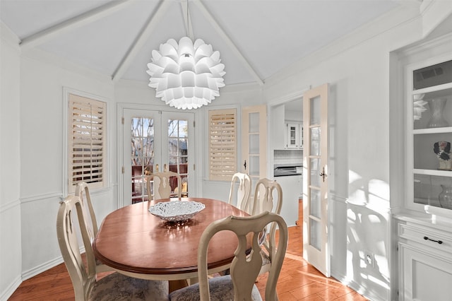 dining area with a chandelier, lofted ceiling with beams, french doors, and light wood-type flooring