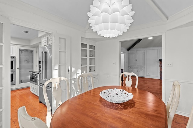 dining space with built in features, light hardwood / wood-style floors, vaulted ceiling with beams, and an inviting chandelier