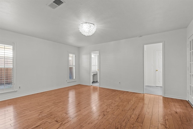 spare room featuring plenty of natural light, light hardwood / wood-style flooring, and a chandelier