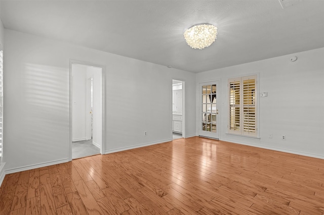 spare room with an inviting chandelier and light hardwood / wood-style floors