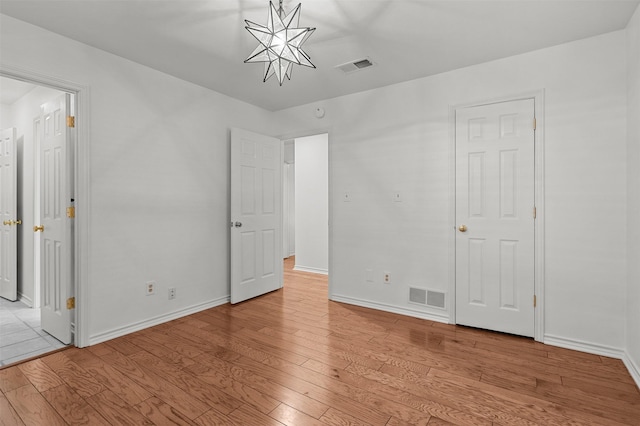 unfurnished bedroom featuring a chandelier and light wood-type flooring