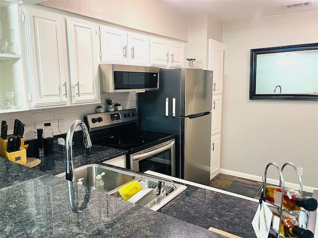 kitchen featuring white cabinets, stainless steel appliances, dark stone counters, and tasteful backsplash