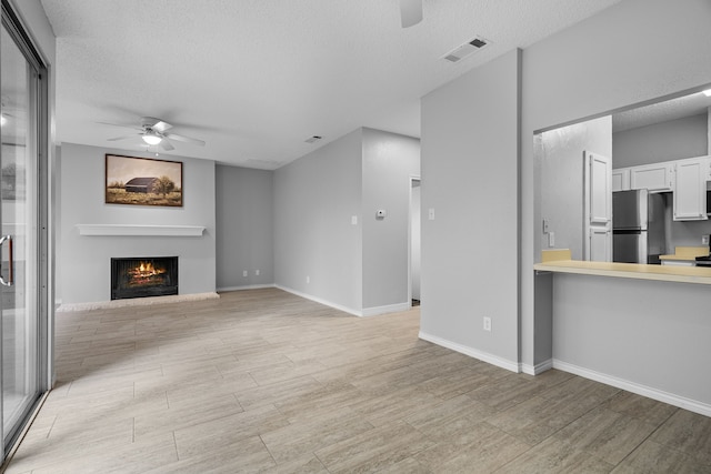 unfurnished living room featuring ceiling fan and a textured ceiling