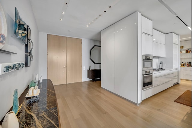 kitchen with white cabinets, light wood-type flooring, track lighting, and appliances with stainless steel finishes