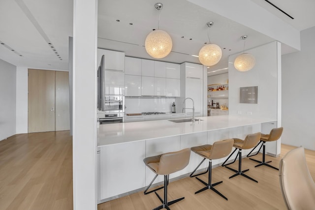 kitchen featuring white cabinetry, hanging light fixtures, kitchen peninsula, a breakfast bar, and light hardwood / wood-style flooring