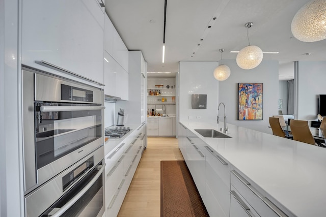 kitchen featuring white cabinets, appliances with stainless steel finishes, decorative light fixtures, sink, and light wood-type flooring