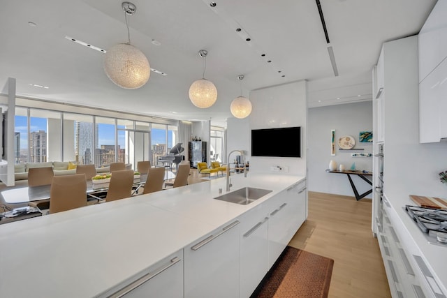 kitchen with light hardwood / wood-style flooring, sink, decorative light fixtures, white cabinets, and expansive windows