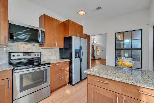 kitchen featuring light stone countertops, a textured ceiling, stainless steel appliances, tasteful backsplash, and light hardwood / wood-style floors