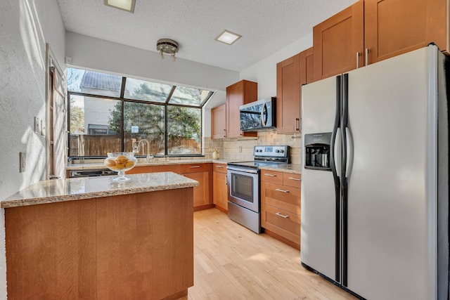 kitchen with a textured ceiling, appliances with stainless steel finishes, light hardwood / wood-style floors, decorative backsplash, and light stone counters