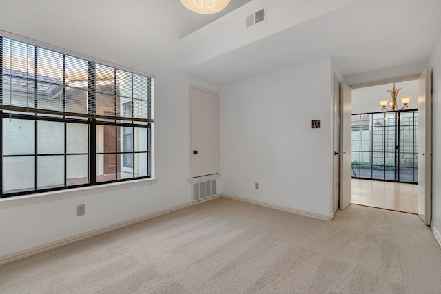 spare room featuring light colored carpet and a notable chandelier