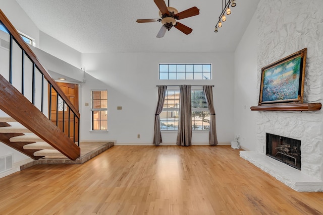 unfurnished living room with a towering ceiling, a textured ceiling, a fireplace, light wood-type flooring, and ceiling fan