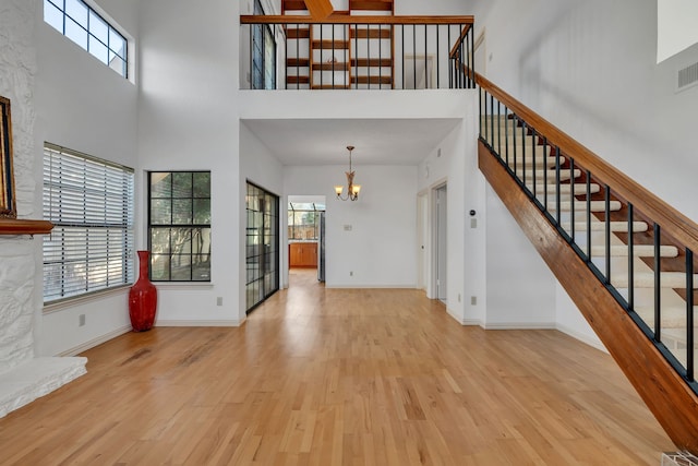 unfurnished living room with light hardwood / wood-style flooring, a towering ceiling, and a notable chandelier