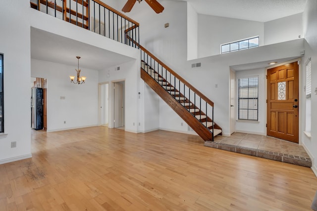 foyer featuring light wood-type flooring, ceiling fan with notable chandelier, and a towering ceiling