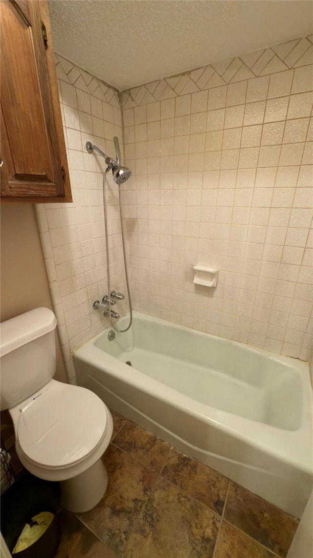 bathroom with a textured ceiling, toilet, and tiled shower / bath