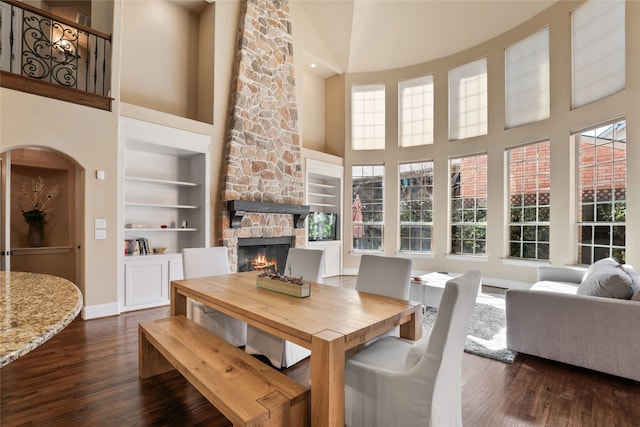 dining space with built in shelves, dark hardwood / wood-style floors, a towering ceiling, and a fireplace