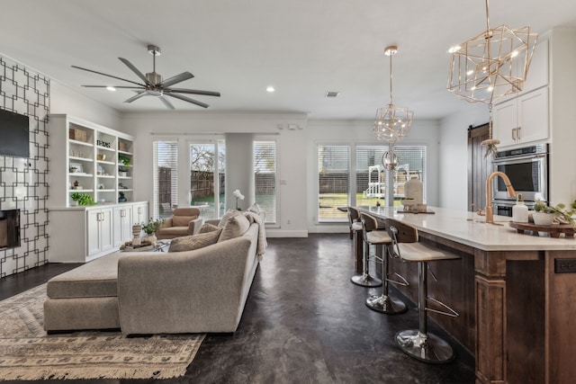 living room featuring crown molding, ceiling fan with notable chandelier, and sink